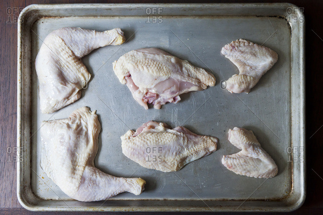 A chicken quartered and laid out on a baking sheet