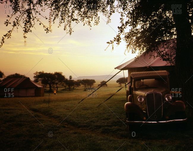 Old car on edge of safari tent camp on Serengeti Plains at dawn