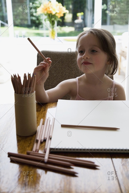 Young girl sitting at a table with a sketch pad and colored pencils