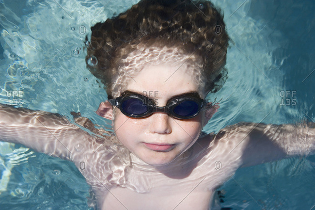 A young boy wearing goggles and floating in water
