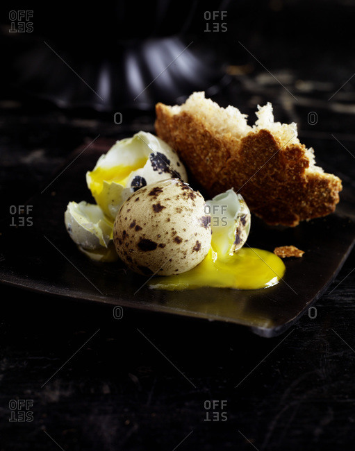 A broken egg with white bread on a black plate.