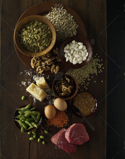 Protein-rich oilseeds, cheese and raw meat on a wooden table from above.