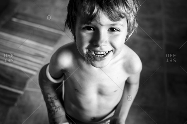 Shaggy haired shirtless boy looking up and smiling.  He\'s wearing\
a cast on left arm