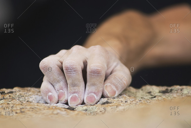 A rock climber\'s fingers grasp a small edge on a granite boulder near Bishop, California