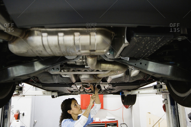Female auto mechanic working under car on hydraulic lift