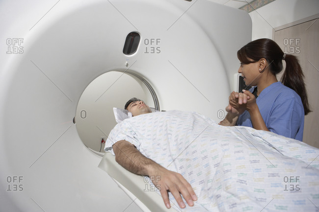 Indian nurse holding patient's hand in MRI scanner