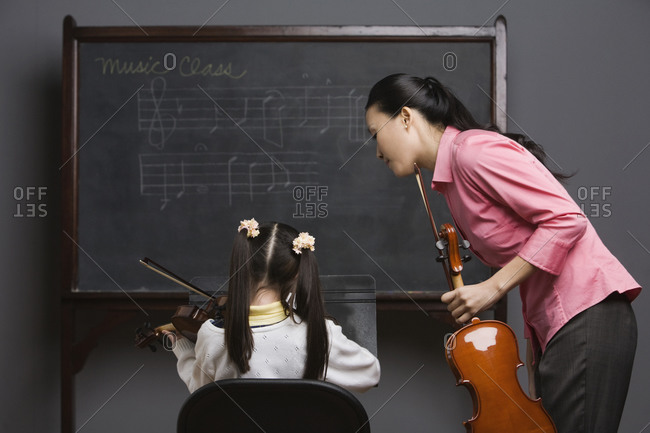 Asian female music teacher watching student play violin
