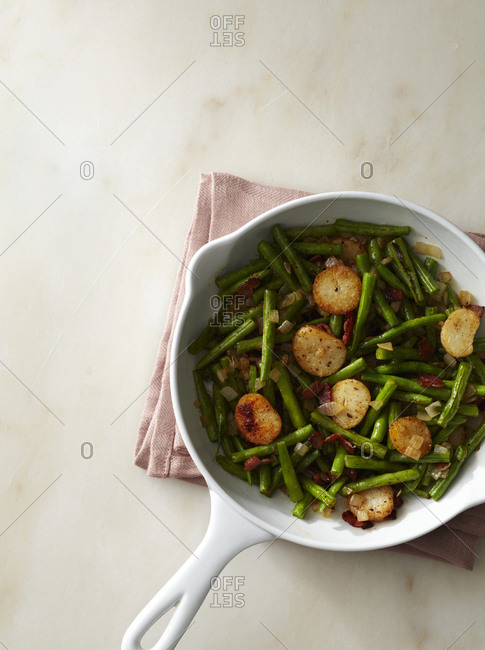 Stewed green bean with roasted potato on a white frying pan from above.