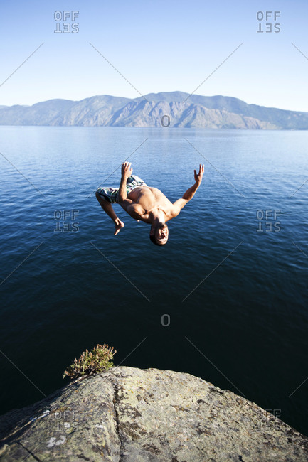 A young man back flips off a cliff into a lake in Idaho.