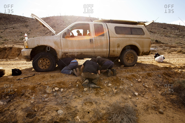 Three male surfers repair a flat tire during a surf trip in Central Baja, Mexico.