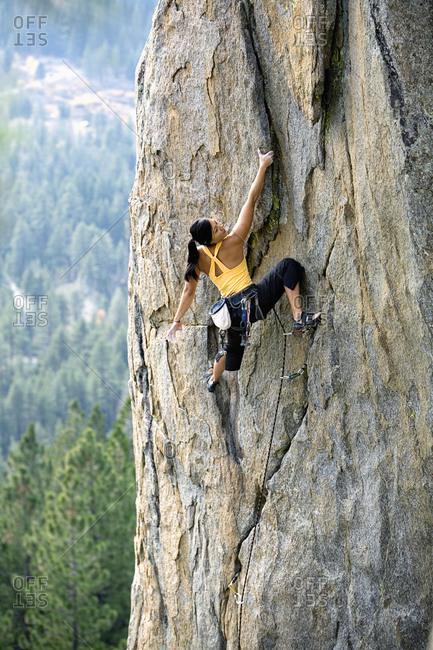 Attractive woman rock climbing high above a valley floor