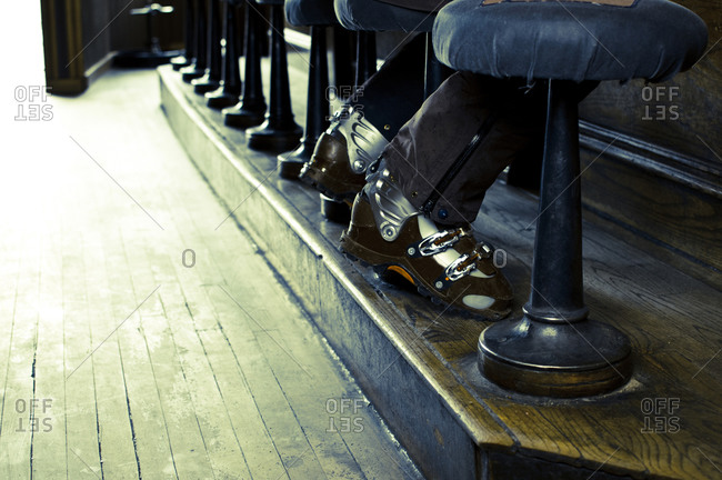 Low angle view of ski boot clad feet seated at a row of bar stools.