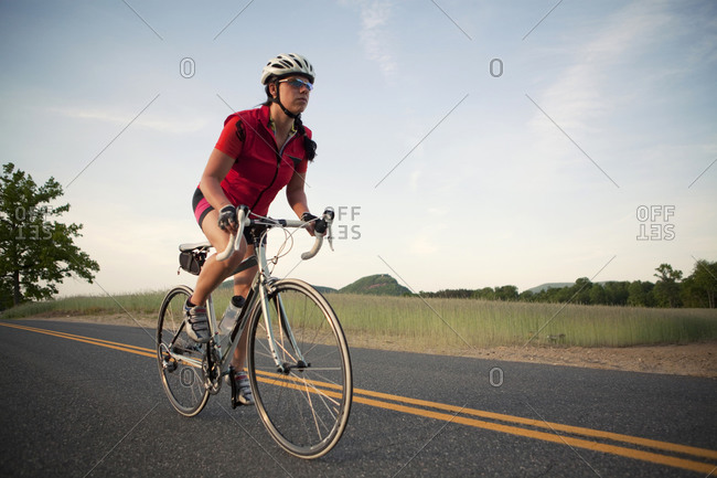 A female cyclist rides on a rural country road in New England.