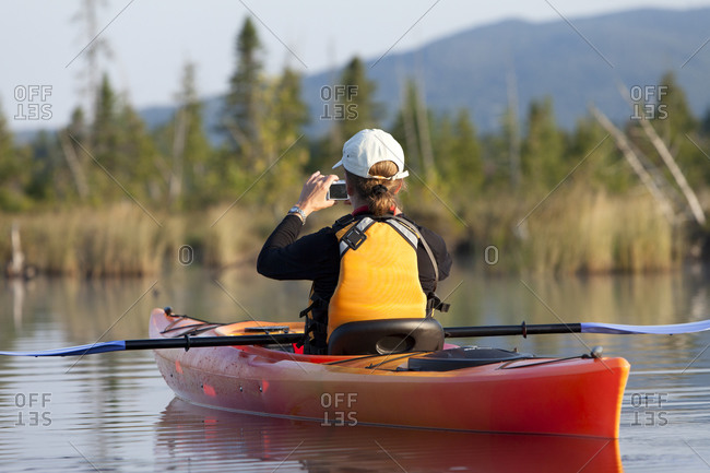 A woman making a photograph while kayaking on Spencer Pond, Maine.