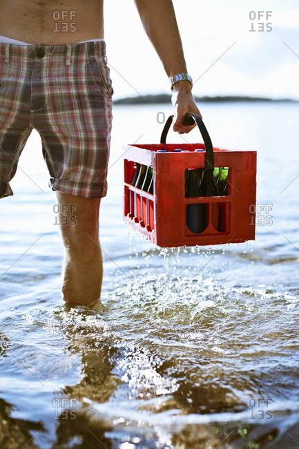 Man in shorts carrying drinks crate in knee deep water