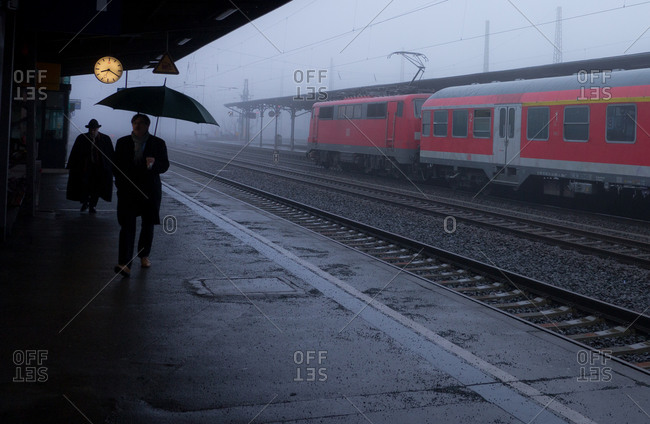 A man with an umbrella at a foggy train station.