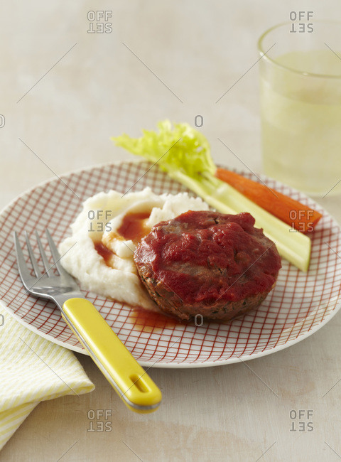 A child\'s plate with a meat loaf patty covered with tomato sauce, mashed potatoes with a celery and carrot stick
