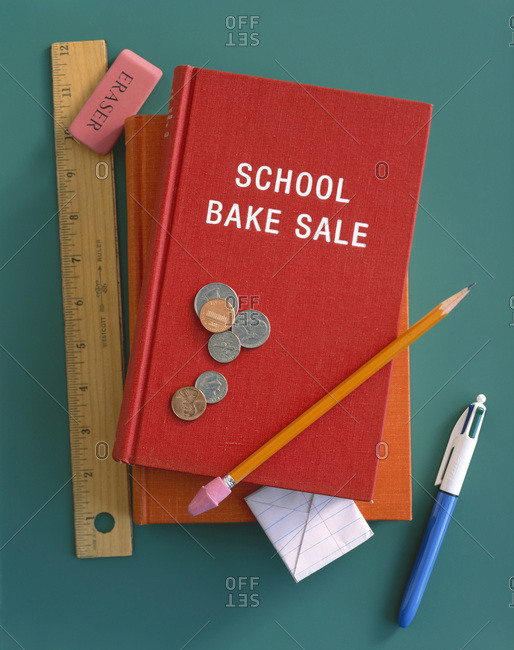 A \'school bake sale\' book with a ruler, eraser, pen, pencil, folded piece of paper and coins