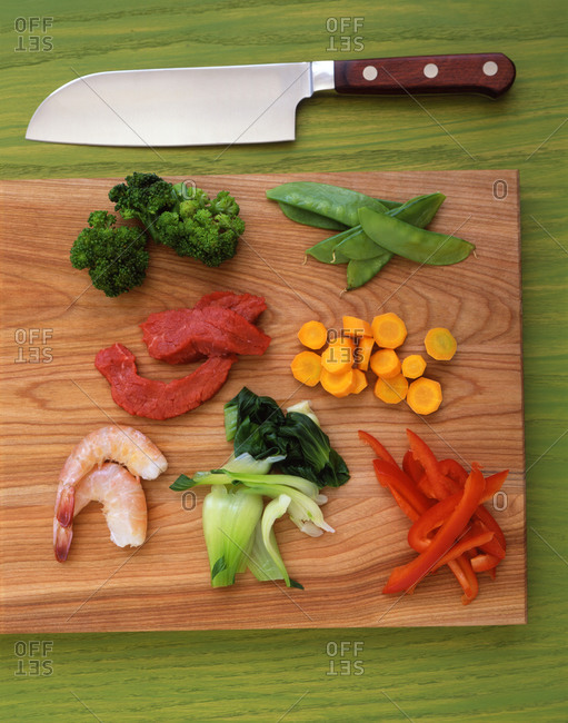 Wooden cutting board and knife with shrimp, beef, broccoli, pak choi, red peppers, carrots and snow peas