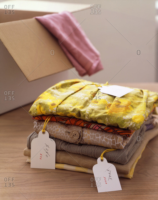 A stack of folded woman�s shirts and blouses with discounted price tags attached, next to a cardboard box