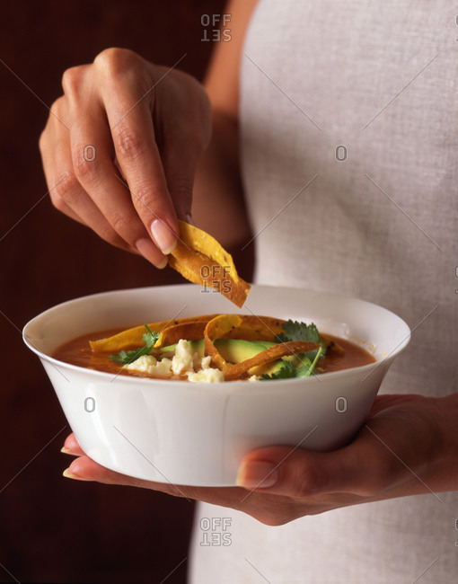 Woman holding a bowl of spicy Mexican tortilla soup topped with tortilla strips