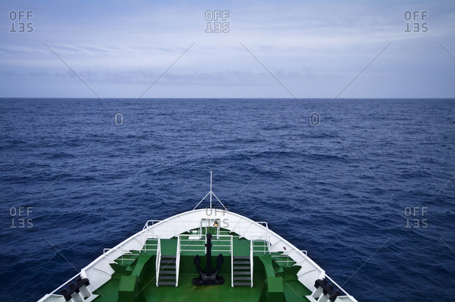 The bow of a ship heading towards a vast and distant ocean horizon