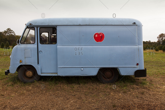Blue painted van with red apple graphic in orchard field