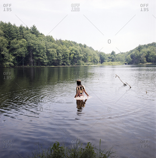 Woman wading into lake, fully clothed in pink dress