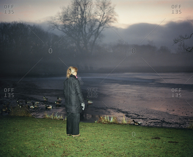 Woman Staring Out At Pond And Ducks In Early Morning Mist
