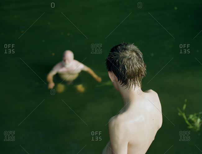A Young Man Watches An Old Man Swimming In A River