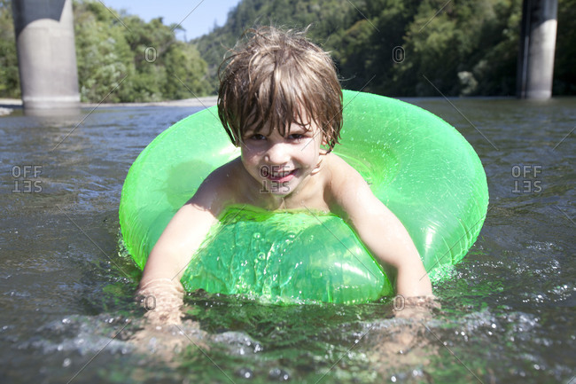 Little child playing in shallow water with green swim ring.