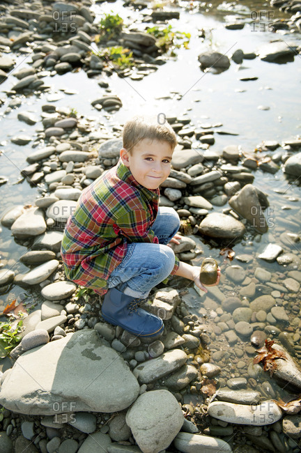 boy playing with rocks next to creek