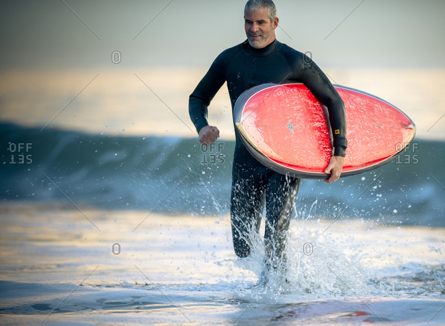 Happy middle aged  man running with surfboard