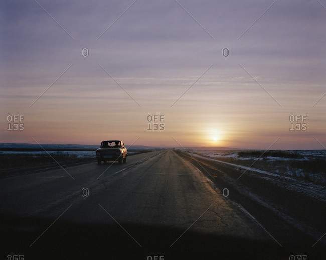 A Russian Travant Car Driving On A Road At Sunset, Seen Through The Windscreen Of A Car Traveling In The Opposite Direction