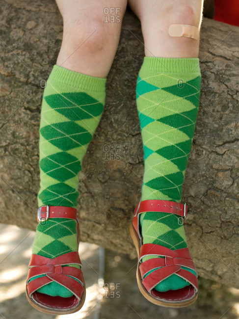 Girl with adhesive bandage on Knee, with Knee Socks and Sandals sitting on large tree branch