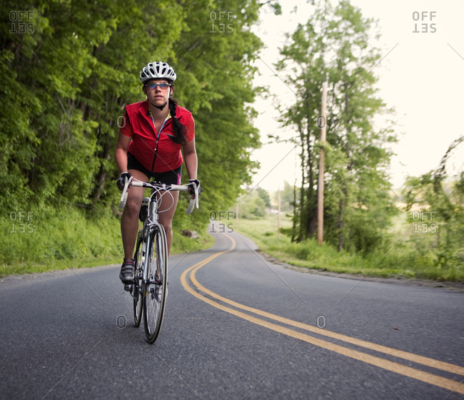 A female cyclist rides on a rural country road in New England.