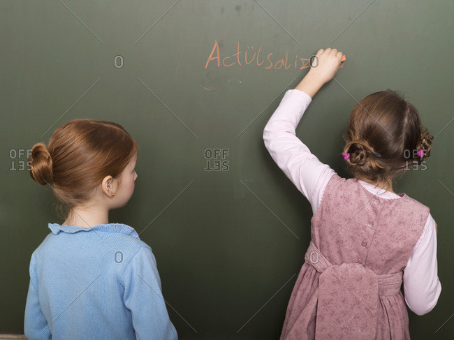 Girls standing in front of blackboard, writing, rear view