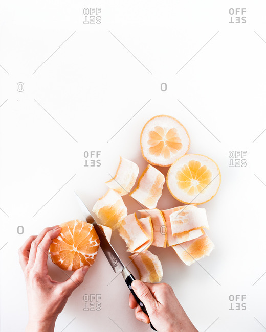 Hands peeling orange with knife on white background