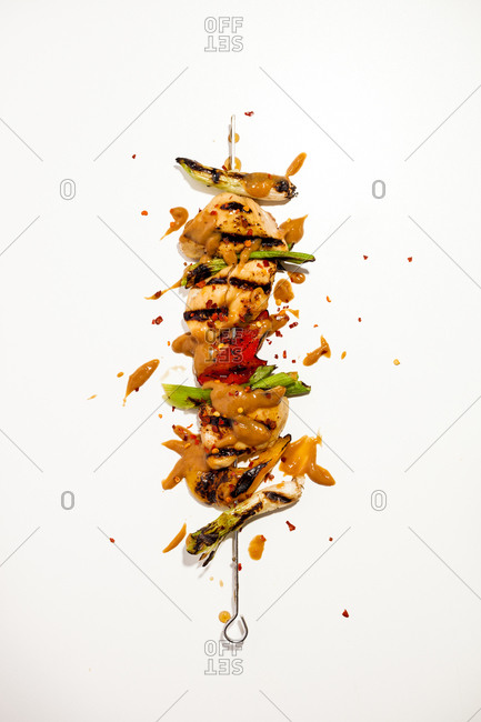 Single skewer of chicken satay with peanut sauce displayed on white background