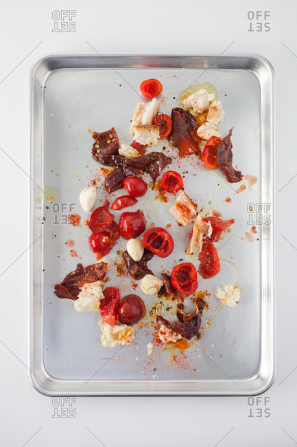 Messy composition with fresh and dried tomatoes, bell pepper, garlic cloves, bread and oil spread on cutting board
