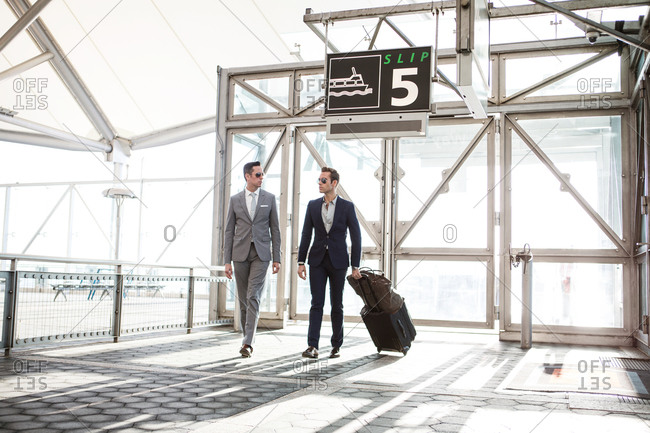 Two young caucasian business men walking, one with suitcase