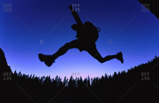 Silhouette of hiker jumping over stream