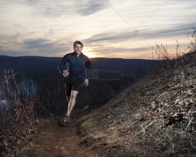 A male trail runner runs across a ridgetop at sunset.