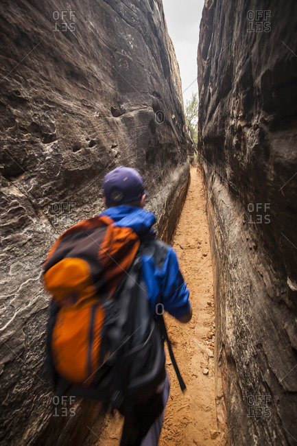 A man with a pack on walking through a narrow canyon while backpacking.