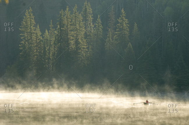A woman rowing a scull boat a foggy morning near  Creede, Colorado.