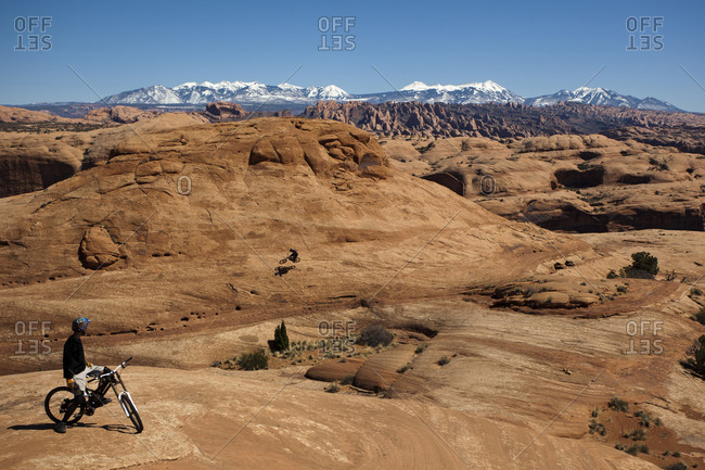 Mountain bikers riding on slickrock in the desert near Moab with mountains in the background.