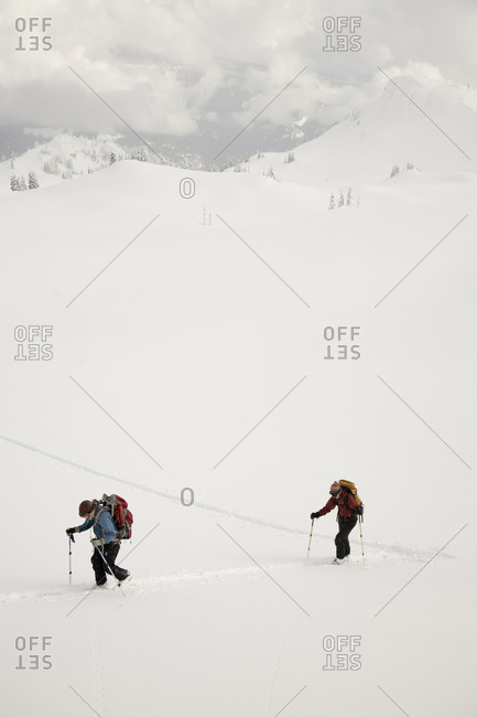 Two female backcountry skiers climb a slope before skiing down.