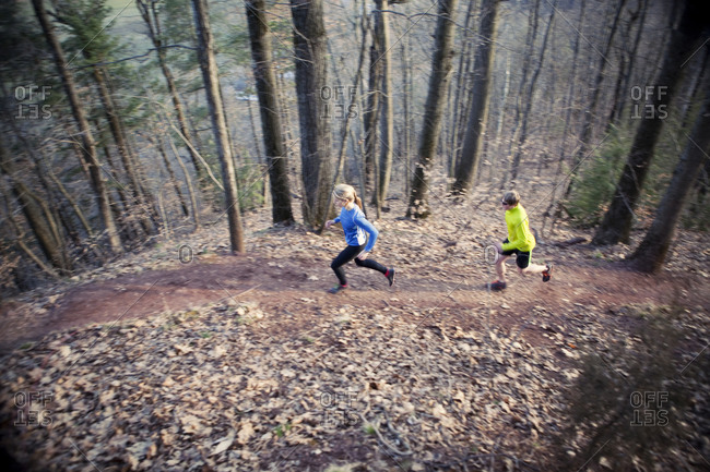 Two trail runners run up a wooded trail on an early spring day.