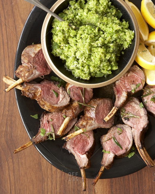 Roasted rack of lamb with lemon wedges and green couscous.