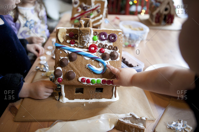 Children decorating gingerbread house with different candies.